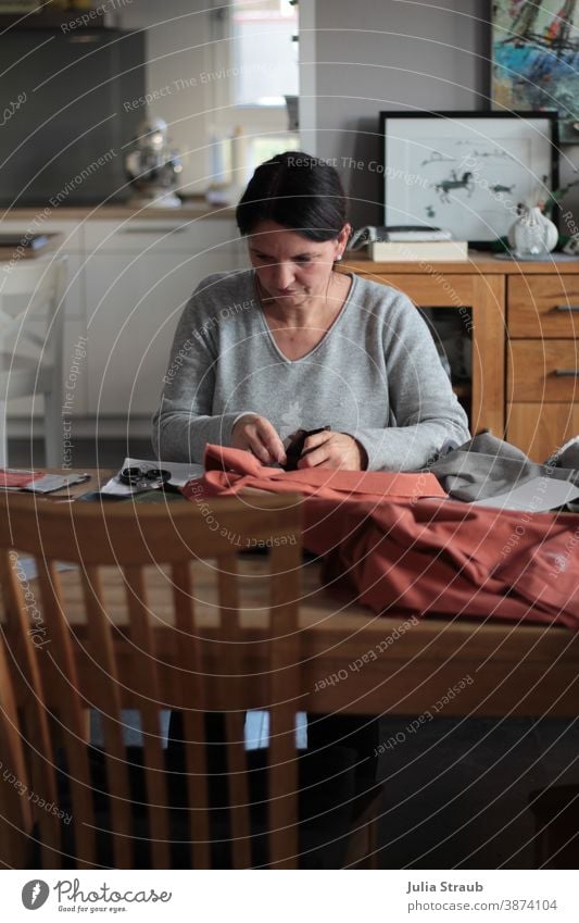 Amateur seamstress sits concentrated at the dining table Dinner table Tailoring Cloth coral natural light Claw fabric scissors Fashion textile Thread Creativity