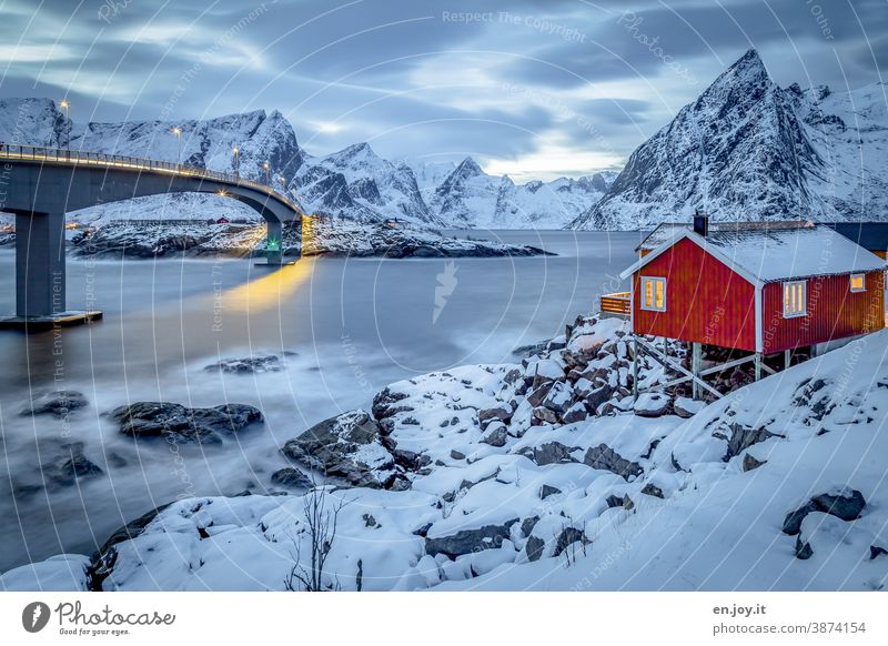 Red wooden house with a view of the Reinefjord and bridge in winter with lots of snow at the blue hour Lofotes Hamnøy Norway Scandinavia North Hut Vacation home
