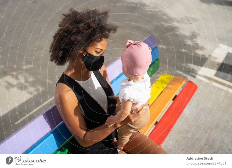 Black woman with cute baby on street mother city stroll bench together coronavirus new normal summer ethnic black african american mask adorable child little