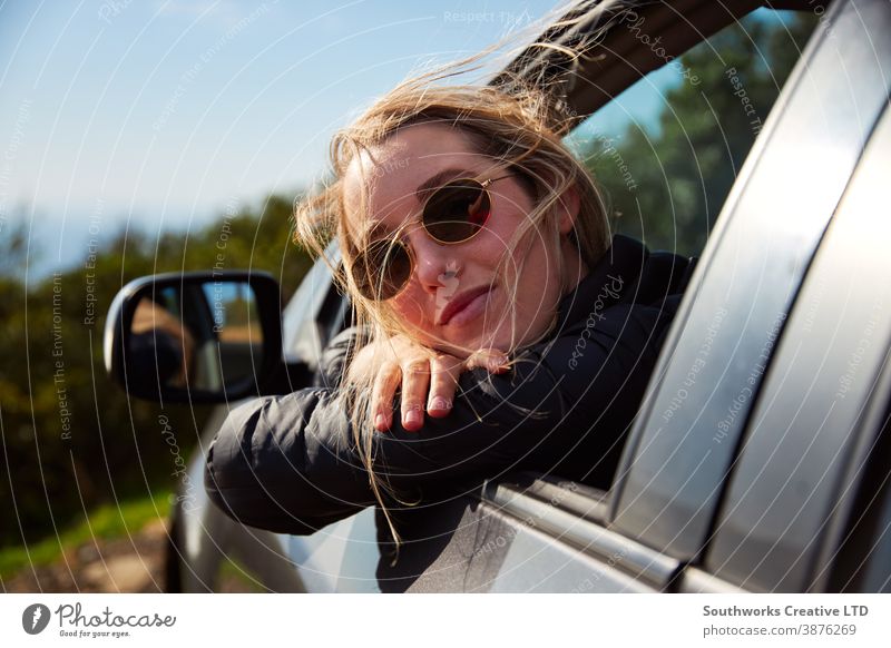 Young Woman On Road Trip Vacation Leaning Out Of Rental Car Window With Mountain Landscape Behind road trip car hire vacation holiday woman young women driving