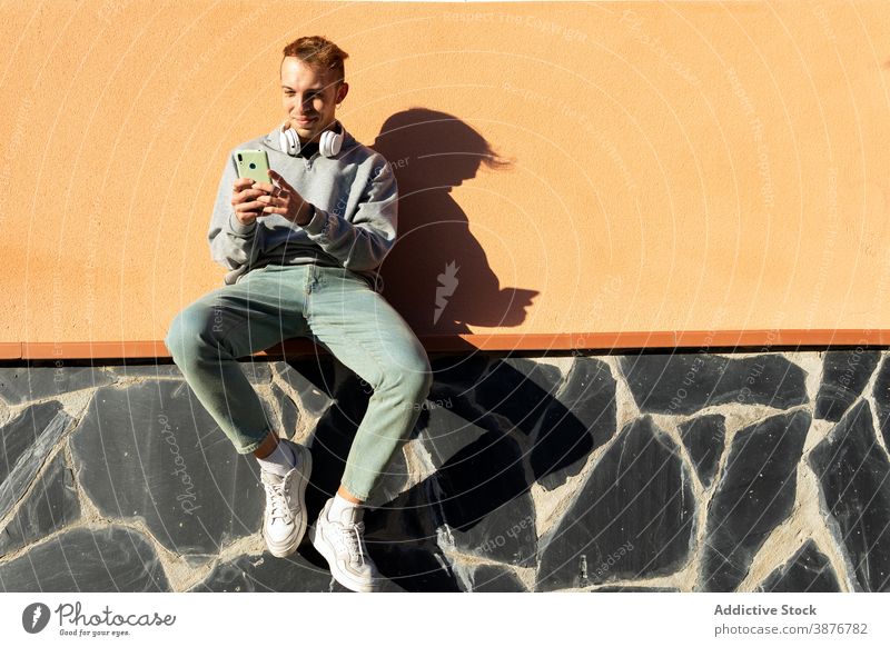 Young hipster man browsing smartphone using wall urban positive online young guy casual headphones mobile sunny shadow gadget connection male lifestyle street