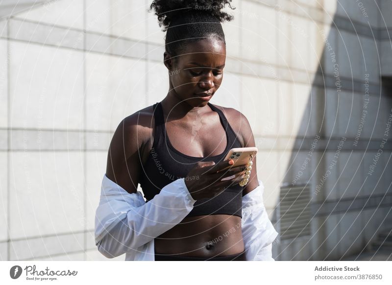 Black sportswoman browsing smartphone in city workout break athlete message training female ethnic black african american street gadget device online