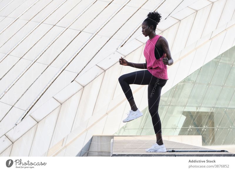 Ethnic sportswoman warming up legs during training warm up city athlete active stretch workout fit female ethnic black african american slim sportswear wellness
