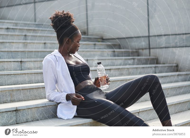 Ethnic sportswoman drinking water in city training runner refreshment thirst sporty female ethnic black african american wellness sportswear healthy rest