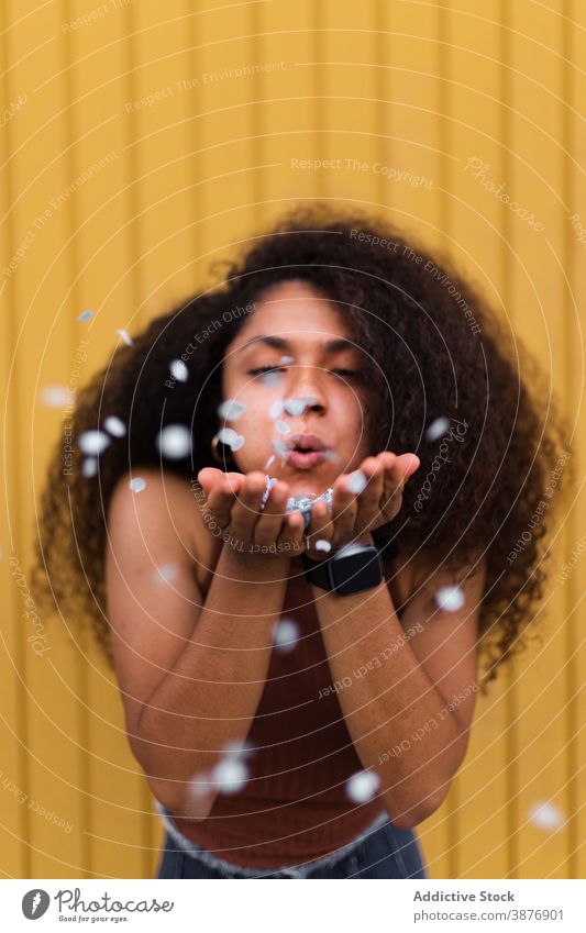 Black woman blowing confetti towards camera festive celebrate concept having fun event curly hair afro female ethnic black african american hairstyle holiday