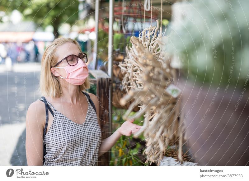 Casual woman shopping outdoor at open market stalls wearing fase masks for protection from corona virus pandemic in Munchen, Germany lifestyle outbreak