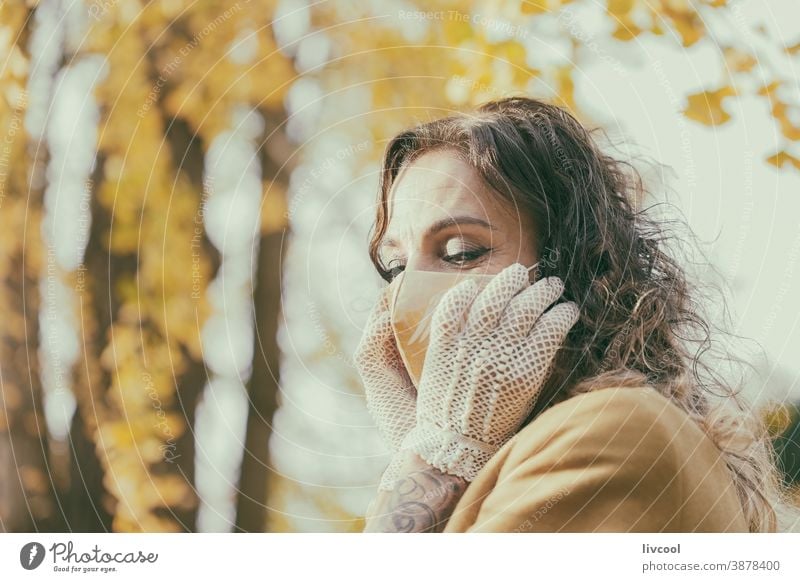 woman with gloves touching her mask yellow park garden yellowish leafs lifestyle mature portrait one people tree coat yellow overcoat scene romantic attitude