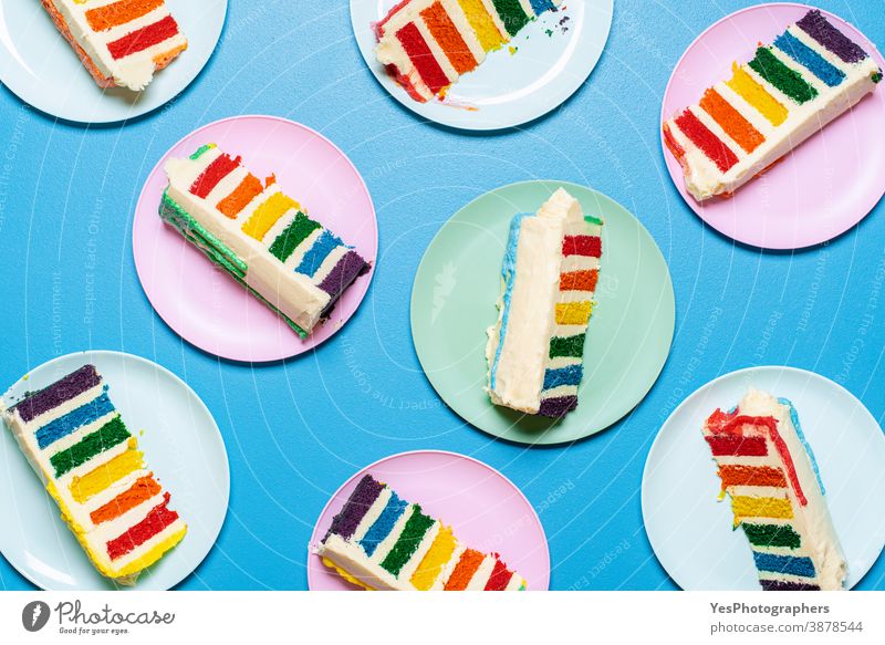 Rainbow cake slices on colorful plates on blue table. Top view of layered cake with buttercream LGBT above view birthday cake blue background celebrate cheerful