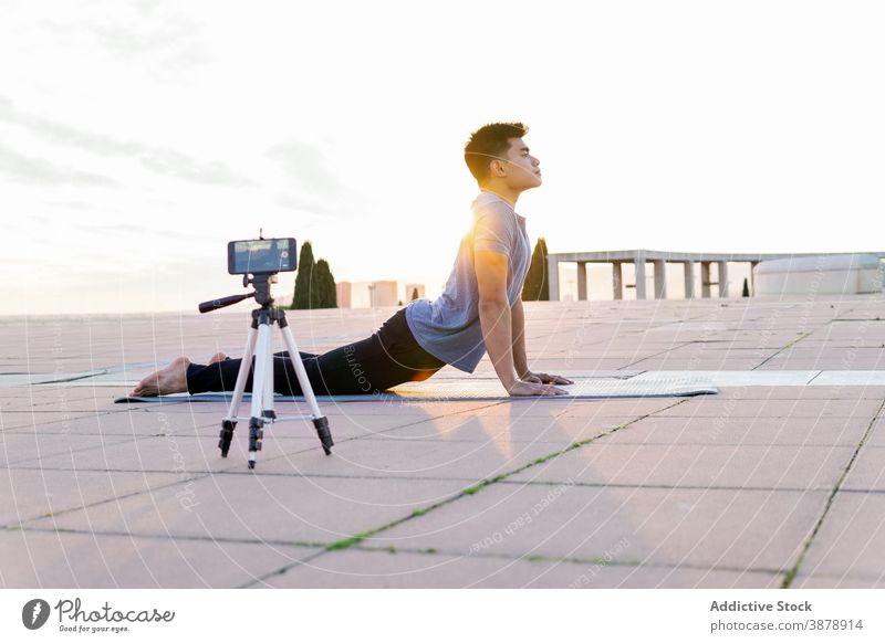 Man doing yoga and recording video on smartphone high cobra pose blogger man practice Bhujangasana influencer backbend male flexible lying mat position body