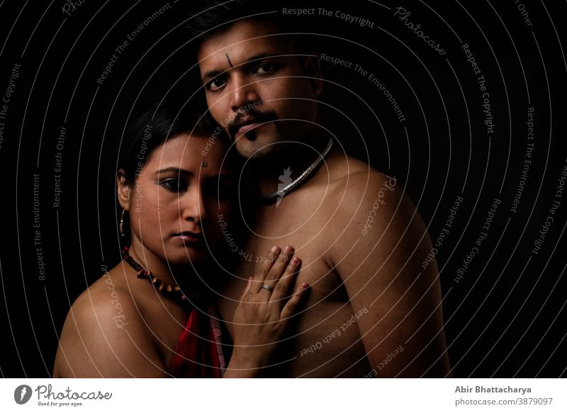 Creative portrait of an Indian dark brunette rural couple standing closely in studio light and shadow with black copy space background. Fashion portrait adult