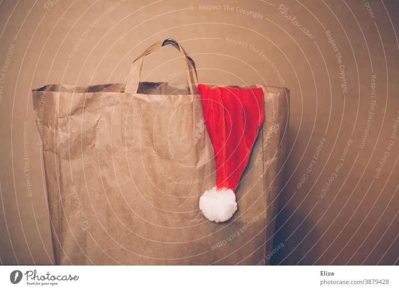 Paper bag with a Santa hat peeping out of it. Christmas shopping. Shopping Santa Claus hat paper bag shopping bag Santa's cap Brown Christmas hat Cap Red