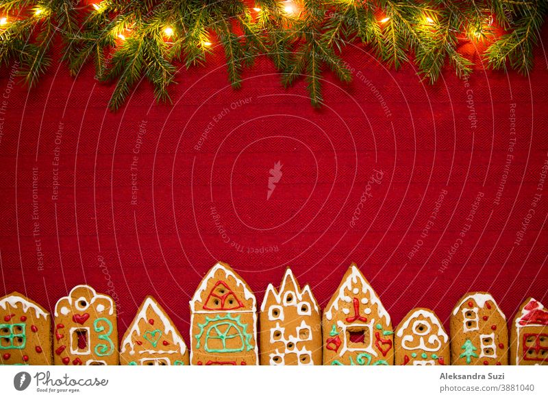 Christmas background. Red table cloth with town of cute gingerbread houses decorated with icing, Christmas lights, glitter. Holiday mood. building card