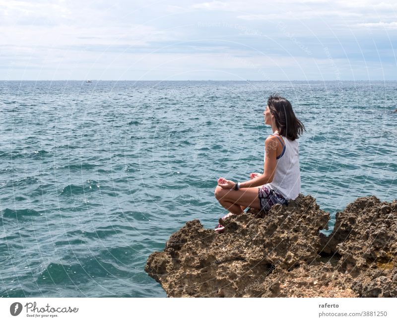 Beautiful woman practicing yoga on the beach at sunrise sitting rock water ocean sea beautiful holiday person girl female lifestyle nature one horizon calm