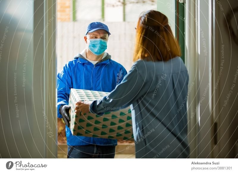 Delivery man bringing holiday packages. Woman at home standing in doorway, receiving parcels for Christmas gifts. Delivery guy in protective mask and gloves.
