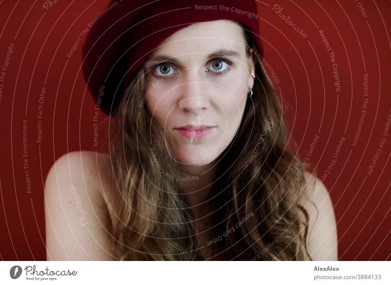 Portrait of a young woman with hat in front of a red wall Woman Slim pretty Brunette long hairs Face smart emotionally see look Looking Direct naturally