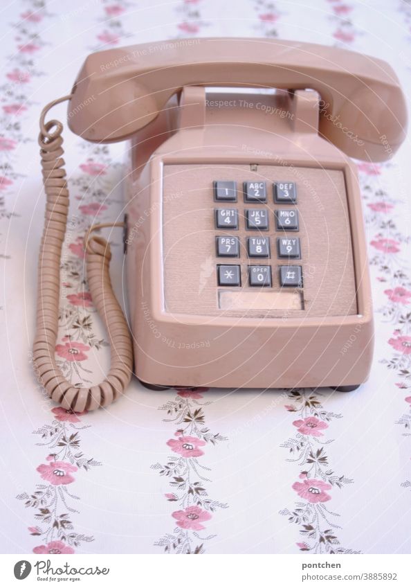 An old telephone in pink stands on a table with a flower pattern. Vintage, progress, technology, communication Telephone vintage Old Pink fumble figures