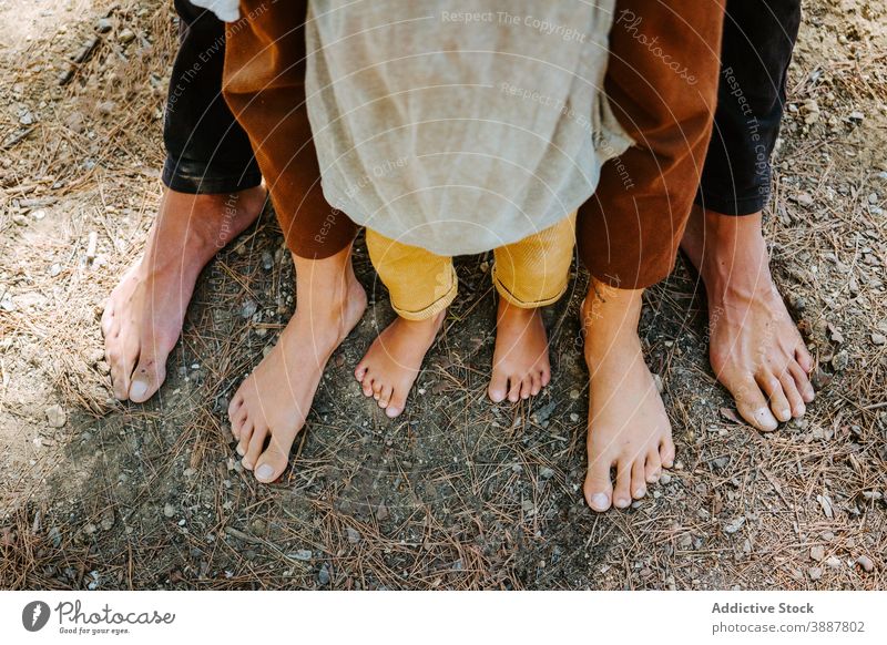 Crop family standing barefoot in woods unity hippie together forest nature bonding couple kid daytime child affection fondness carefree support trust