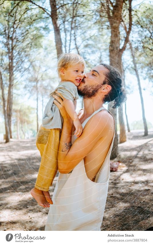 Happy father kissing cute kid in forest child cheek love tender together weekend ethnic multiracial diverse parenthood fatherhood adorable hipster enjoy