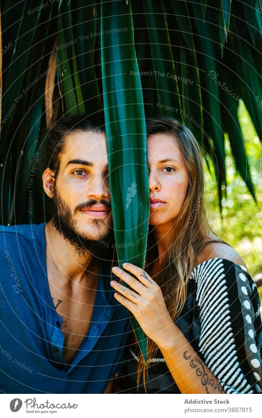 Couple in tropical garden looking at camera couple hide plant leaf laugh entertain multiethnic multiracial diverse exotic park summer together relax positive