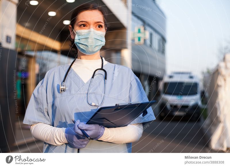 Young female doctor in front of emergency services ambulance or hospital aid care carer caucasian clinic clipboard concerned corona coronavirus covid covid19