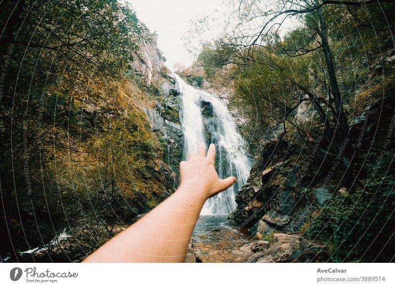 Horizontal shot of an out of focus hand reaching a massive waterfall nature tree western serene scenery natural peaceful foliage landscape cascade forest