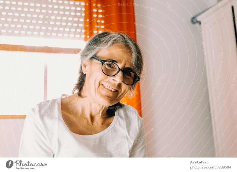 Close up of a old woman with glasses smiling to camera in a bright bedroom person grandmother lady mature pensioner senior smile looking portrait 50s clinic