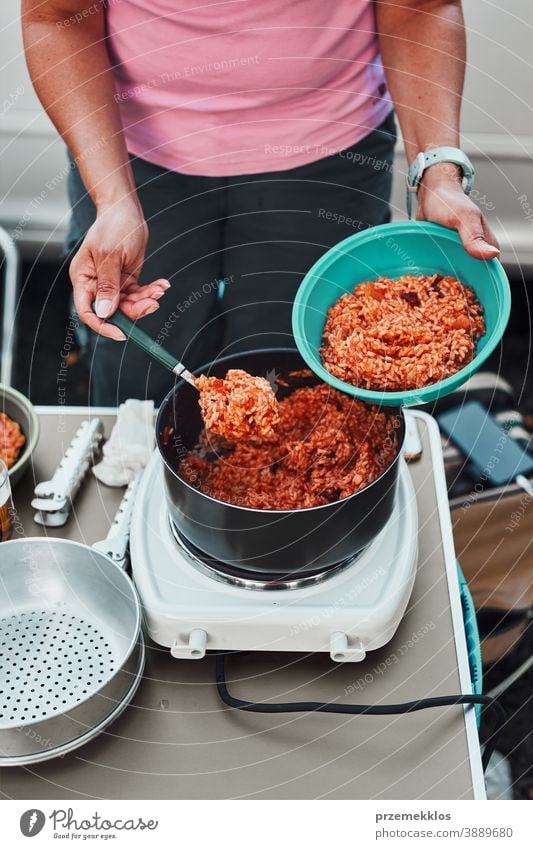 Woman putting rice dish with tomato sauce to a bowl on summer vacations on camping lunch outdoor cooking cuisine hot pot meal female dinner eating recreation