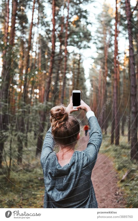 Young woman taking photos using smartphone during walk in a forest on summer vacation trip active activity destination enjoy exploration female hike lifestyle