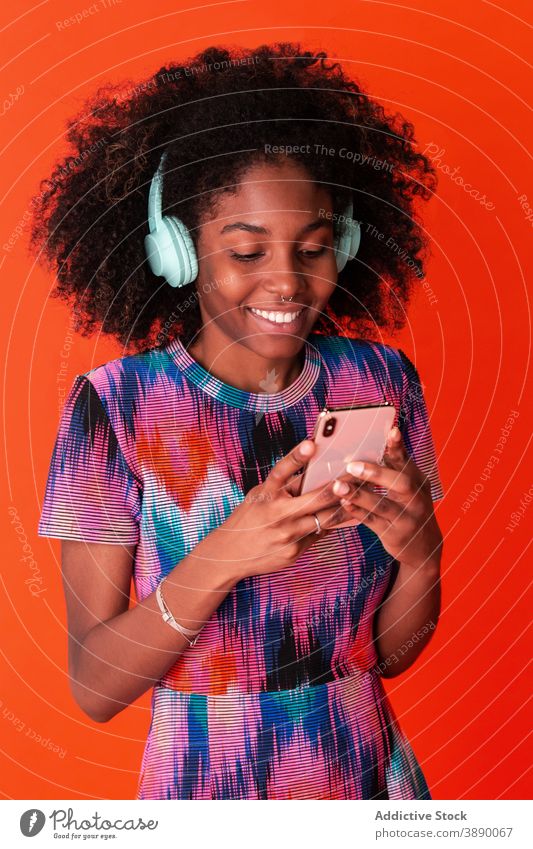 Cheerful black woman using smartphone and headphones music model bright style modern millennial selfie studio gadget listen vivid content casual social media