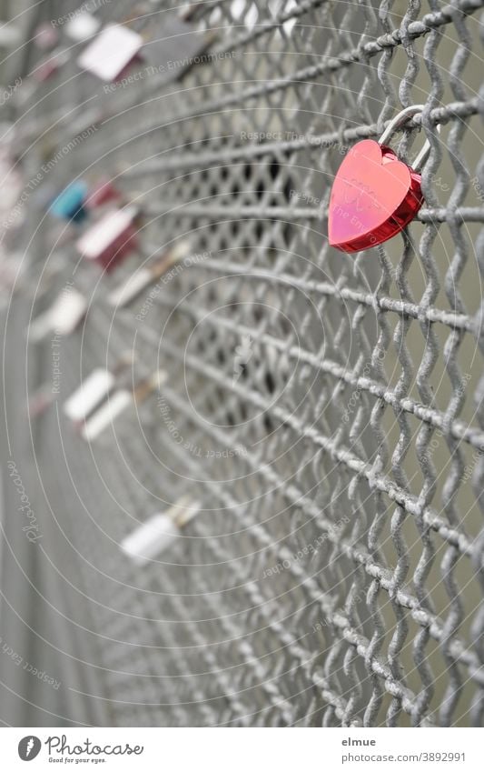 A red heart castle in the foreground and other love castles in the background are attached to a bridge railing / expression of love / ritual heart-lock