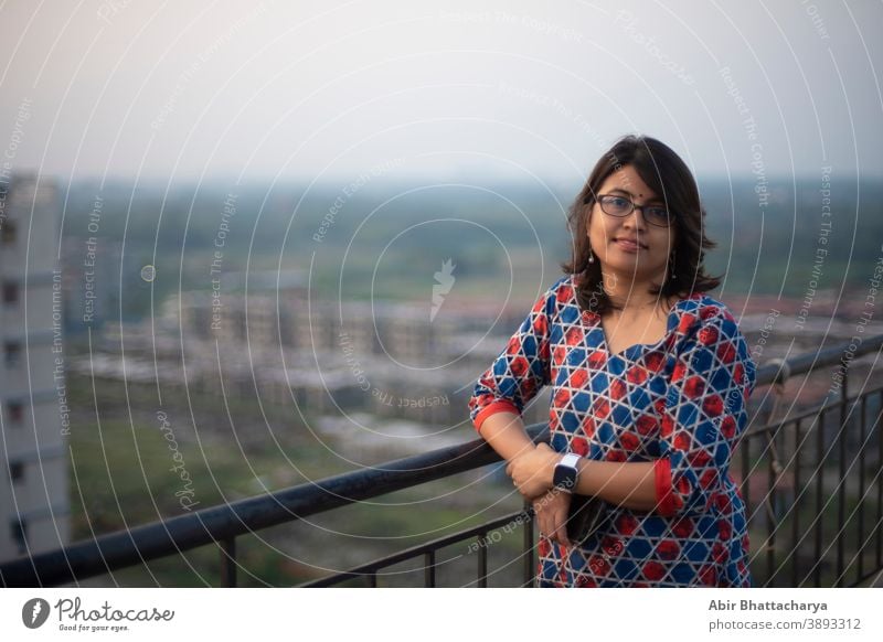 Portrait of an Indian Bengali brunette young woman in traditional wear standing on rooftop/balcony in the afternoon in urban background. Indian lifestyle adult