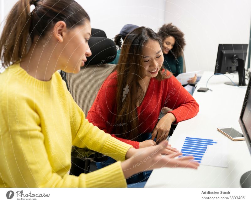Young female colleagues discussing charts in office work diagram casual positive women business together workplace coworker multiethnic multiracial diverse