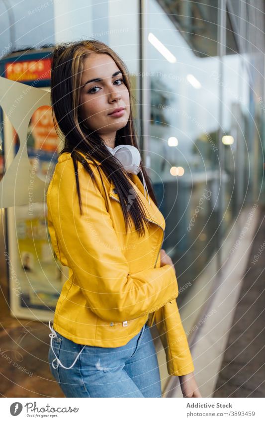 Young woman in yellow jacket standing on street trendy leather jacket style colorful bright modern calm urban young female millennial lifestyle glass wall