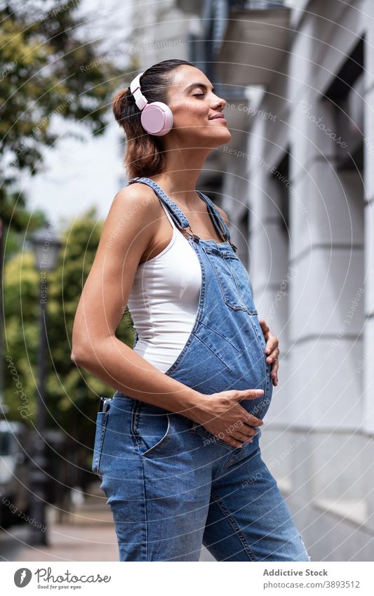 Carefree pregnant woman listening to music in city pregnancy carefree touch belly headphones female wireless street prenatal tummy device lady eyes closed await