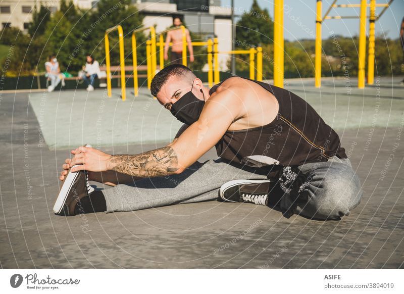 Young man with face mask stretching before calisthenics training sport warm up athlete coronavirus new normal pandemic facial mask muscles strength gymnastics