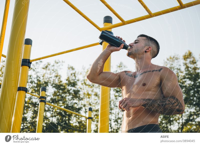 Young urban athlete drinking water at a calisthenics gym outdoor sport man bottle muscles strength gymnastics street freestyle body shirtless aesthetic tattoo