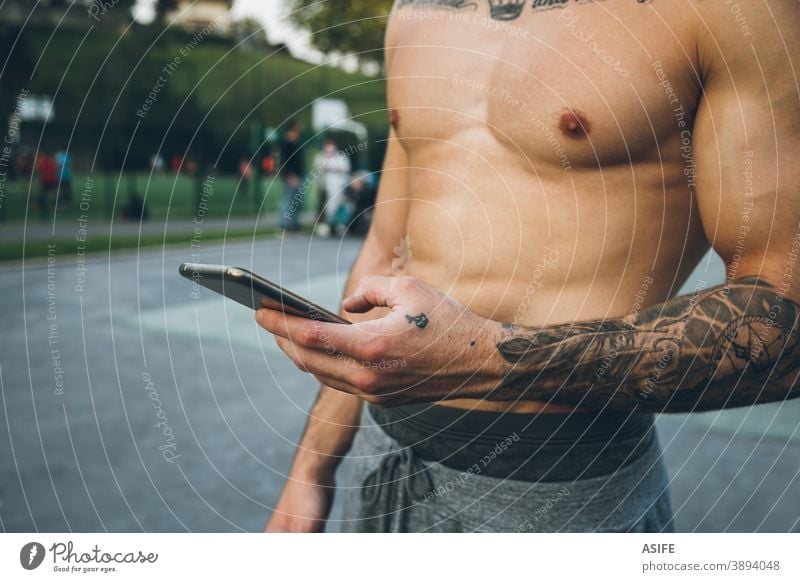 Young urban bodybuilder with tattoos using his smart phone during calisthenics training hands athlete man muscles mobile phone telephone arm sport strength