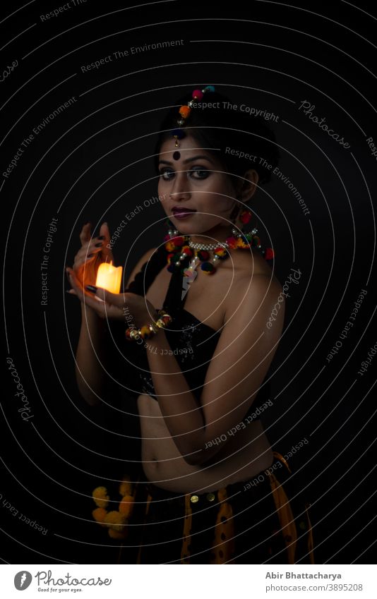 Portrait of Indian Bengali brunette woman in Indian traditional tribal/ villager dress and handmade ornaments with candle in dark copy space studio background. Indian lifestyle and fashion photography.