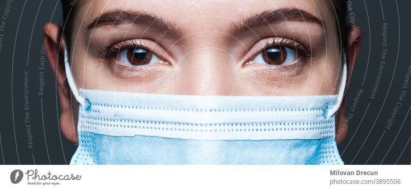 Young caucasian woman wearing blue surgical face mask closeup wide screen portrait coronavirus covid-19 female eyes doctor banner clinic disease epidemic fear