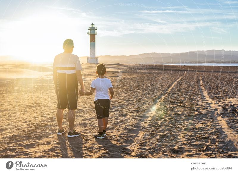 Grandfather and grandson looking a lighthouse on the beach at sunset back boy child childhood children coast dad day elderly family fangar far del fangar fun