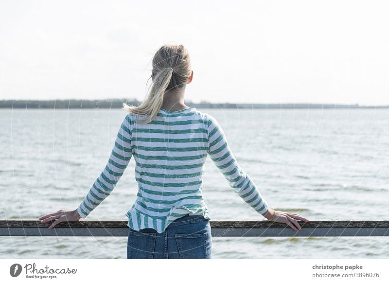 Blonde woman stands at rehling and looks at the sea Woman Rear view Ocean vacation Baltic Sea Bodden Bodden landscape Mecklenburg-Western Pomerania relax
