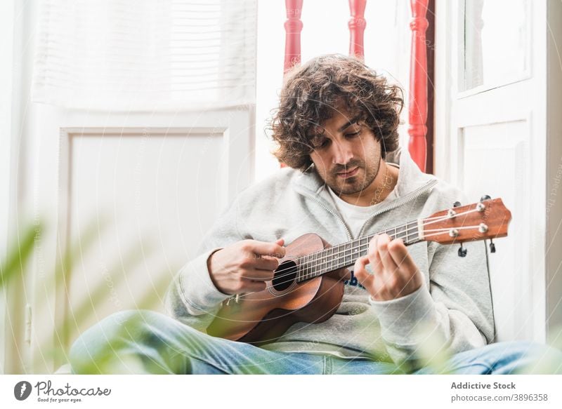 Pensive man playing ukulele guitar cheerful musician perform positive instrument young ethnic hispanic male melody home lifestyle song sound acoustic guitarist