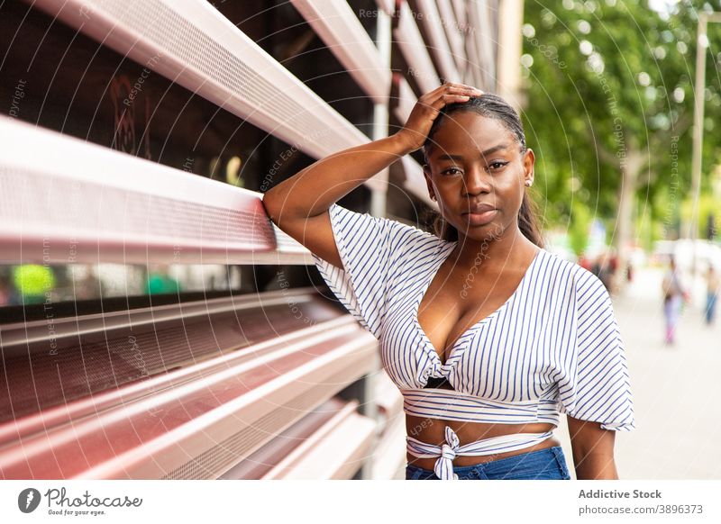 Black woman in stylish wear looking at camera on street style trendy outfit modern urban stripe young summer female african american black ethnic calm relax