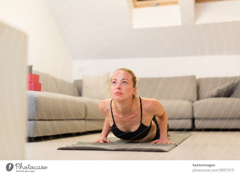 Beautiful blonde woman doing home workout indoors. Woman practice yoga at  home. Fit girl using workout tutorials for healthy active lifestyle. Woman  using quarantine for home workouts. - a Royalty Free Stock