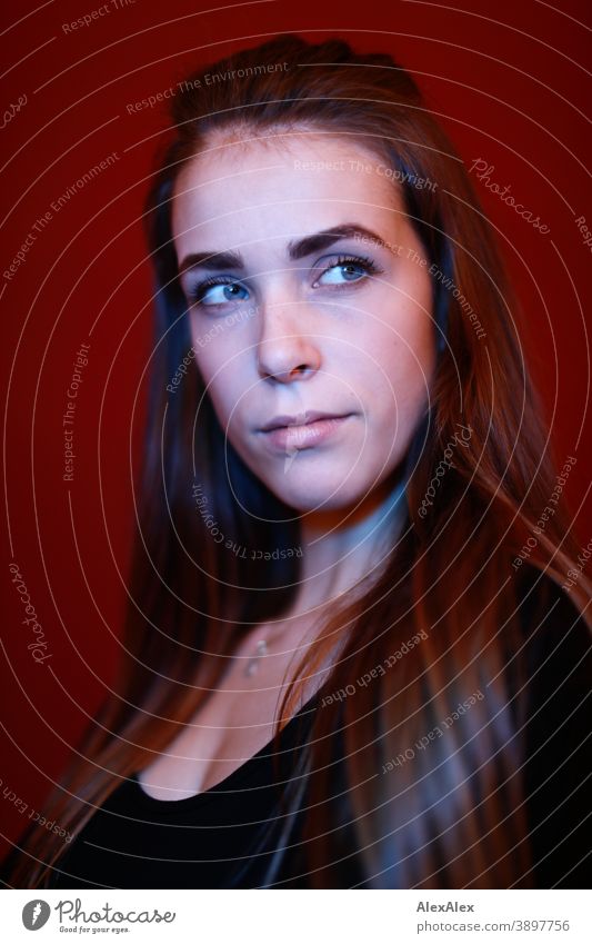 Portrait of a young woman in a room in front of a red wall with red and blue light Student daintily Jewellery Facial expression empathy Looking into the camera