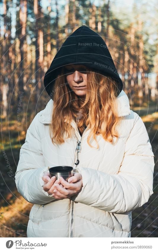 Woman in a hood having break during autumn trip holding cup with hot drink from thermos flask on autumn cold day active activity adventure coffee destination