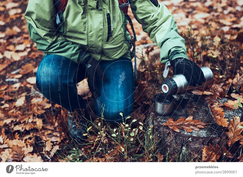 Woman with backpack having break during autumn trip on autumn cold day pouring a hot drink from thermos flask outdoors destination hiking holiday vacation hiker