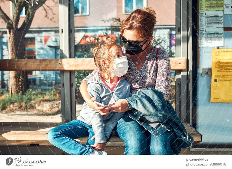 Woman and her child waiting for a bus sitting at bus stop of public transport woman mask face pandemic coronavirus outbreak protection girl parent daughter