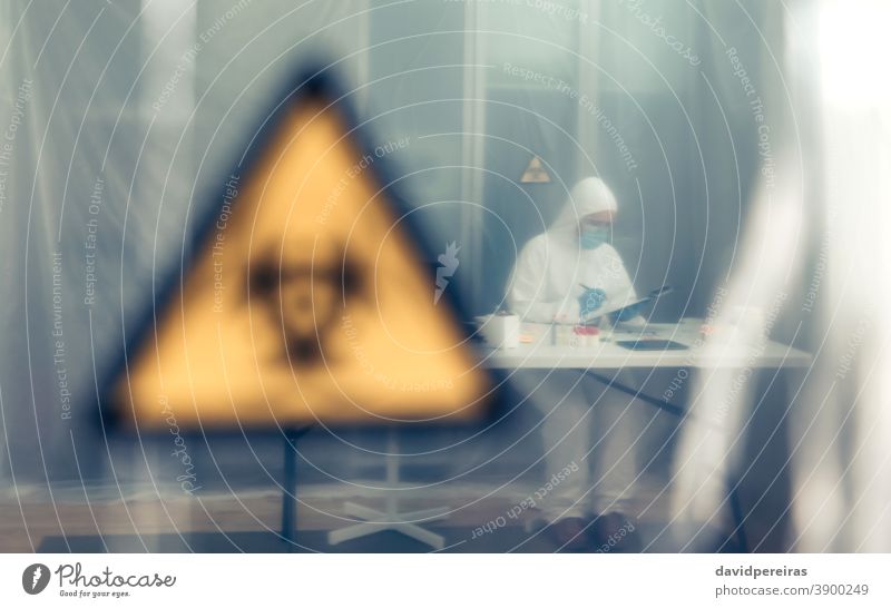 Scientist investigating in the laboratory behind a protective curtain protection curtain scientist isolation coronavirus biohazard symbol