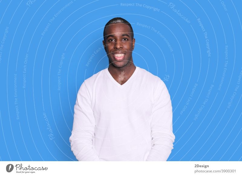 Smiling young african american man guy in casual white sweater posing isolated on pastel blue background studio portrait. People sincere emotions lifestyle concept. Mock up copy space. Looking camera.